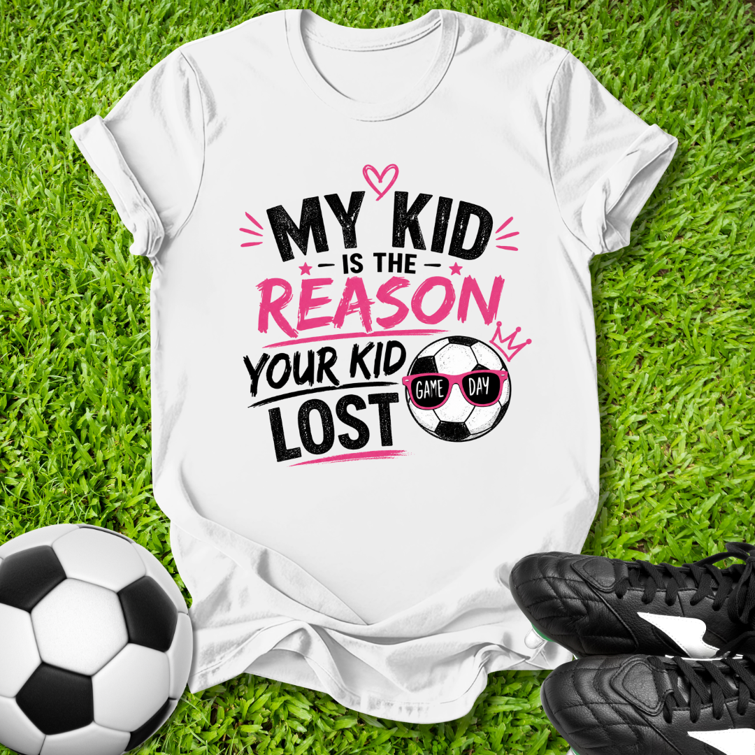 White t-shirt with humorous soccer-themed text on grass with soccer ball and shoes.
