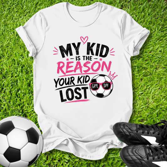 White t-shirt with humorous soccer-themed text on grass with soccer ball and shoes.