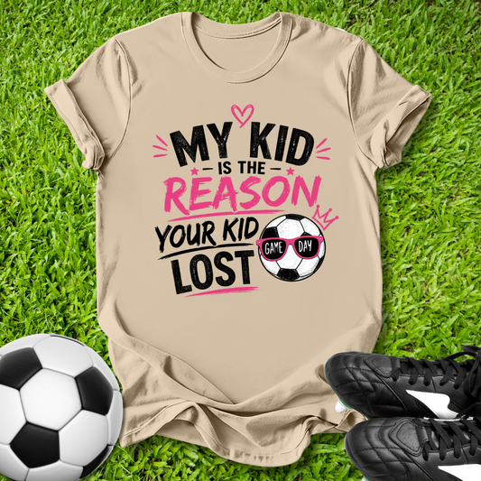 Beige t-shirt with humorous soccer-themed text on grass with soccer ball and shoes.