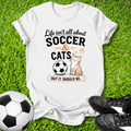 White t-shirt that says life isn't about soccer & cats but it should be with a cat and a soccer ball on a soccer field.