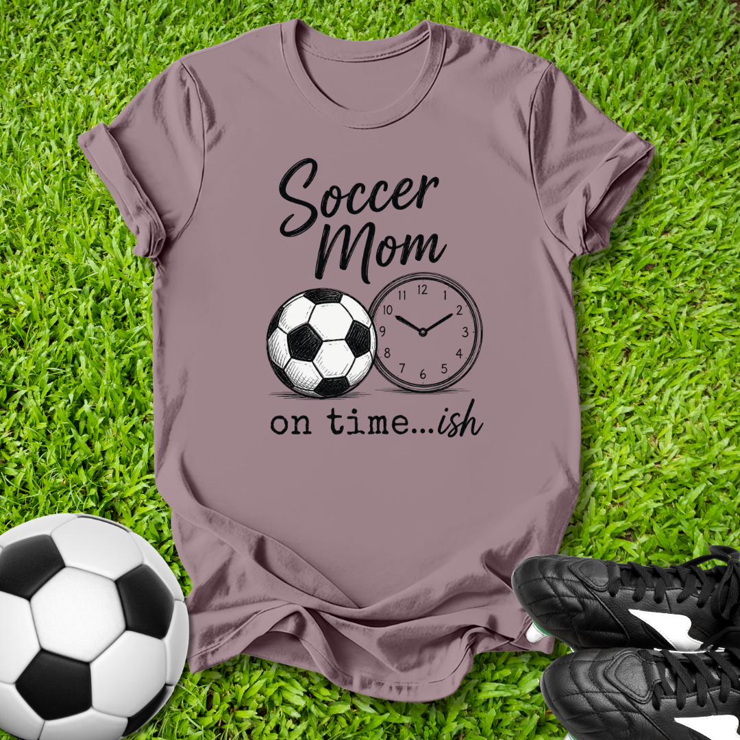 Purple t-shirt with 'Soccer Mom on time...ish' design on grass with soccer ball and shoes.