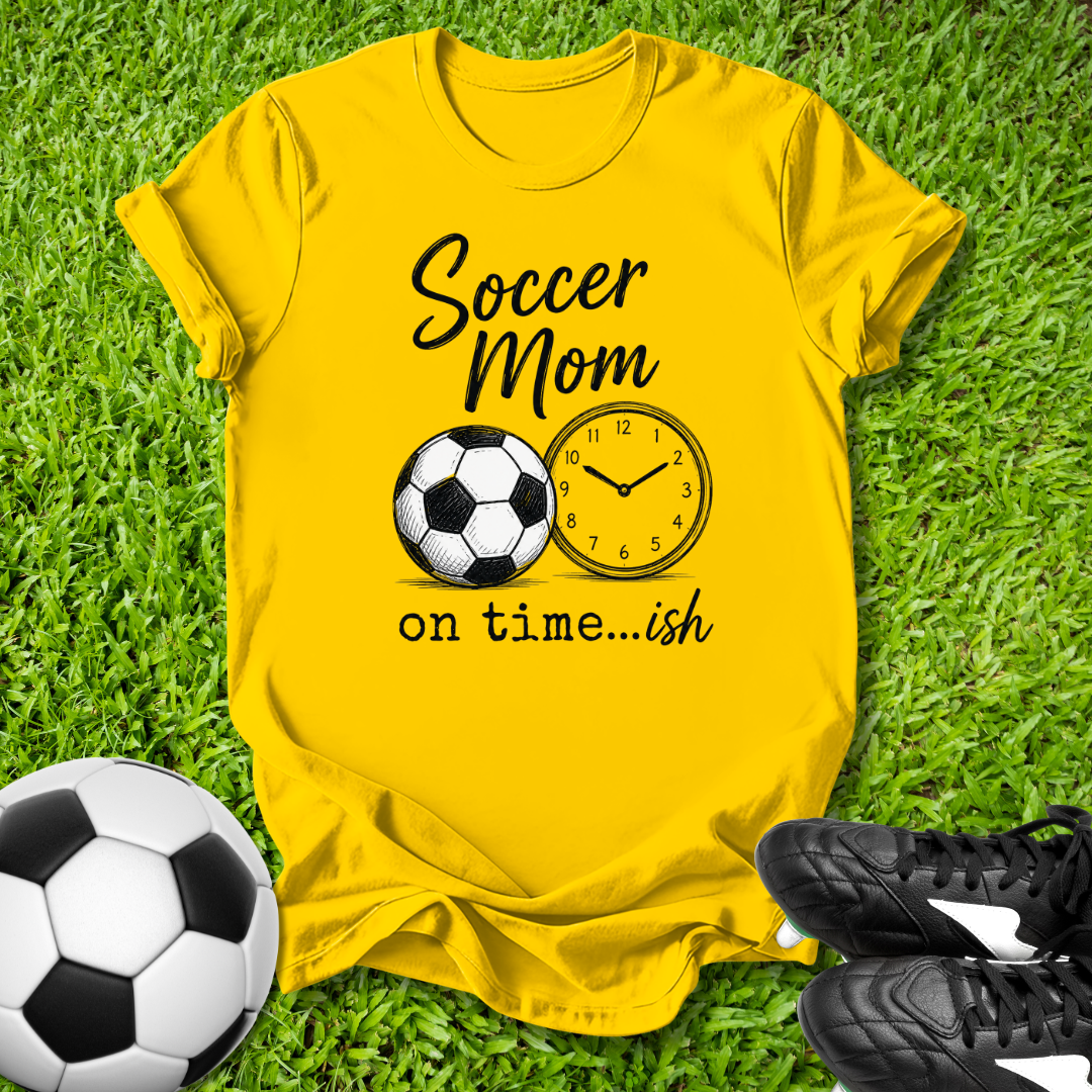 Yellow t-shirt with 'Soccer Mom on time...ish' design on grass with soccer ball and shoes.