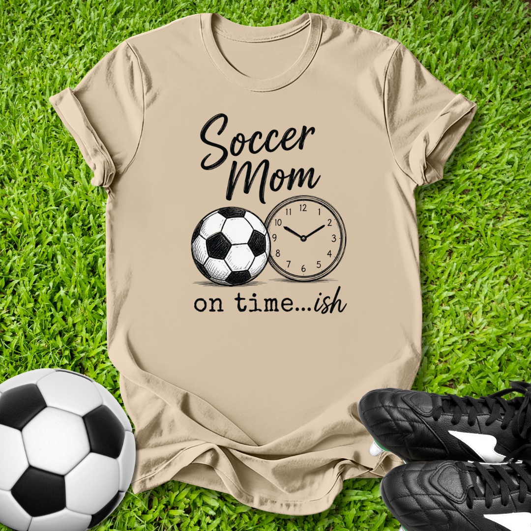 Beige t-shirt with 'Soccer Mom on time...ish' design on grass with soccer ball and shoes.