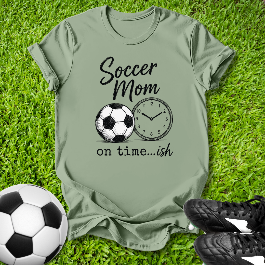 Green t-shirt with 'Soccer Mom on time...ish' design on grass with soccer ball and shoes.