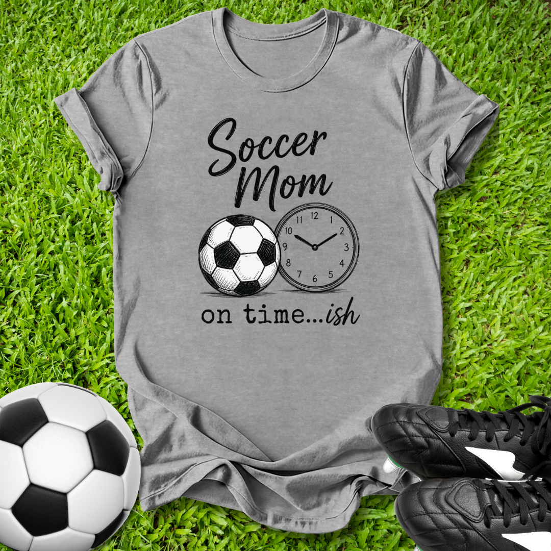 Gray t-shirt with 'Soccer Mom on time...ish' design on grass with soccer balls and shoes.