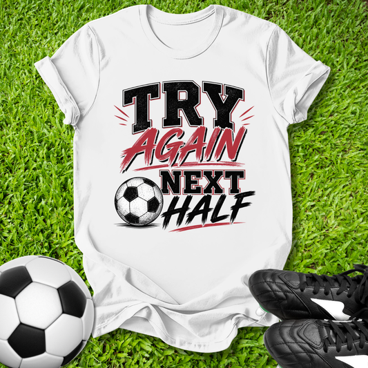 White t-shirt with 'Try Again Next Half' text on grass with soccer ball and shoes