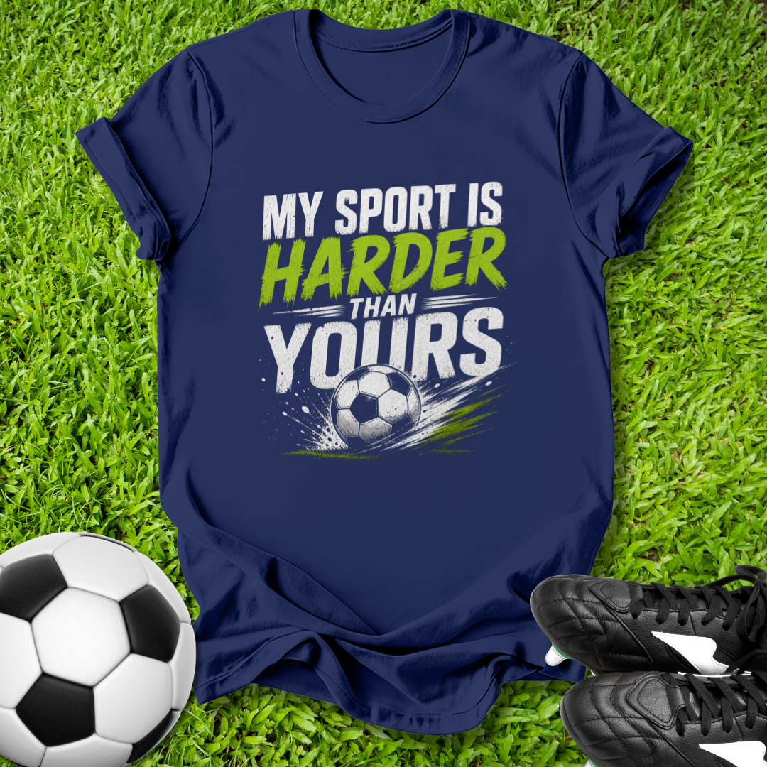 Navy blue t-shirt with 'My sport is harder than yours' text on grass with soccer ball and shoes.