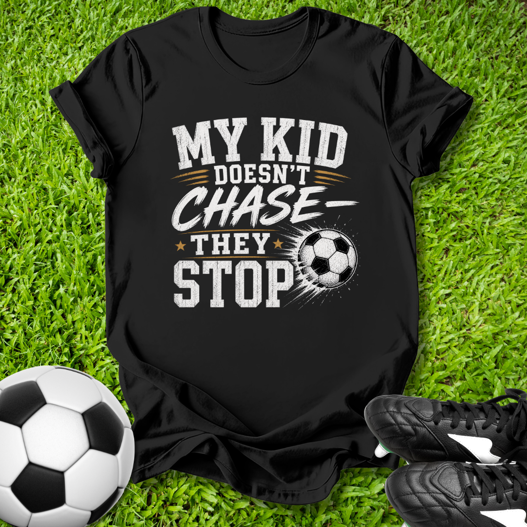Black t-shirt with soccer-themed shirt with a soccer ball that says in white text y Kid Doesn't Chase--They stop. text on grass with soccer ball and shoes