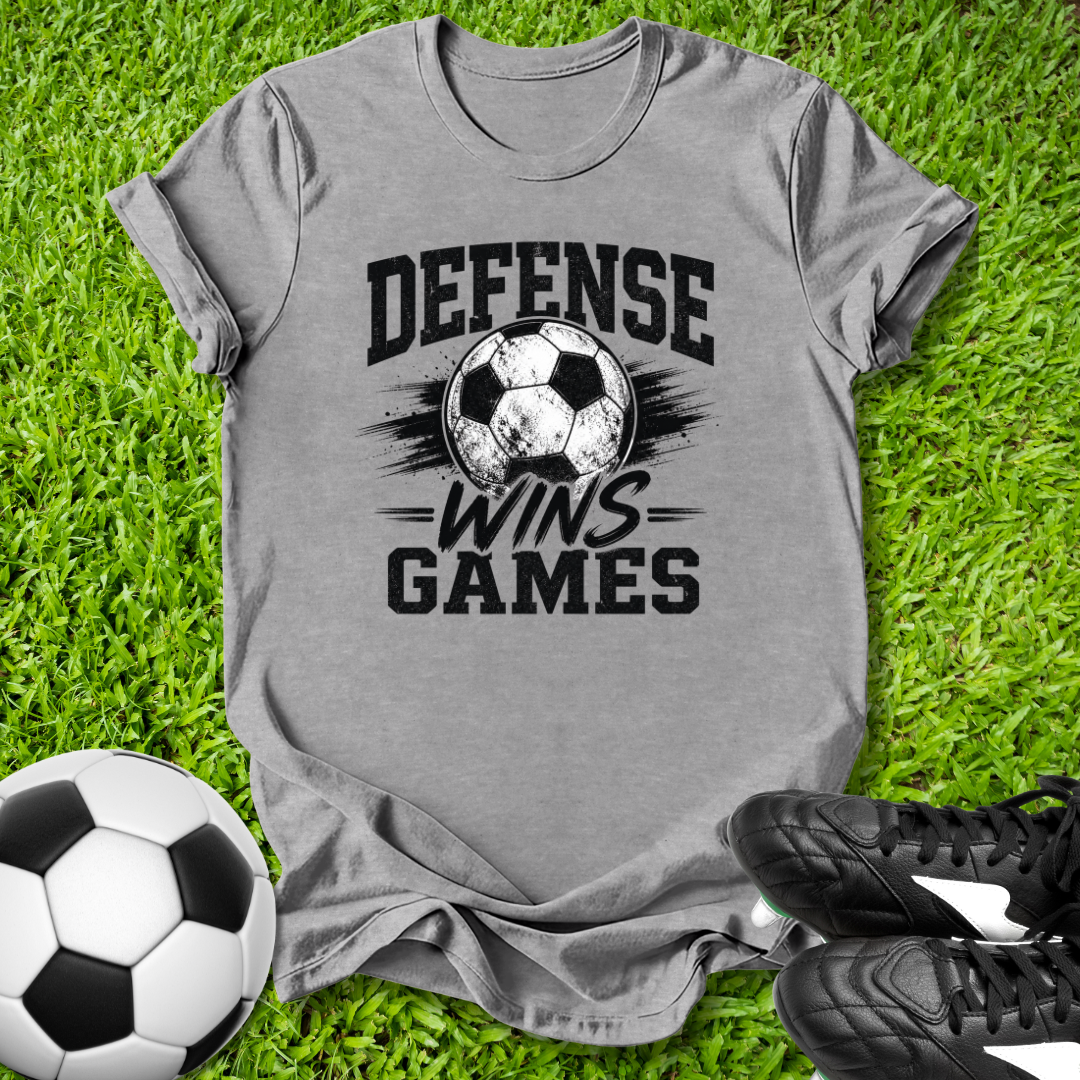 Gray t-shirt with 'Defense Wins Games' text and soccer ball graphic on grass with soccer balls and shoes.