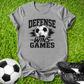 Gray -shirt with 'Defense Wins Games' text and soccer ball graphic on grass, with soccer ball and shoes.