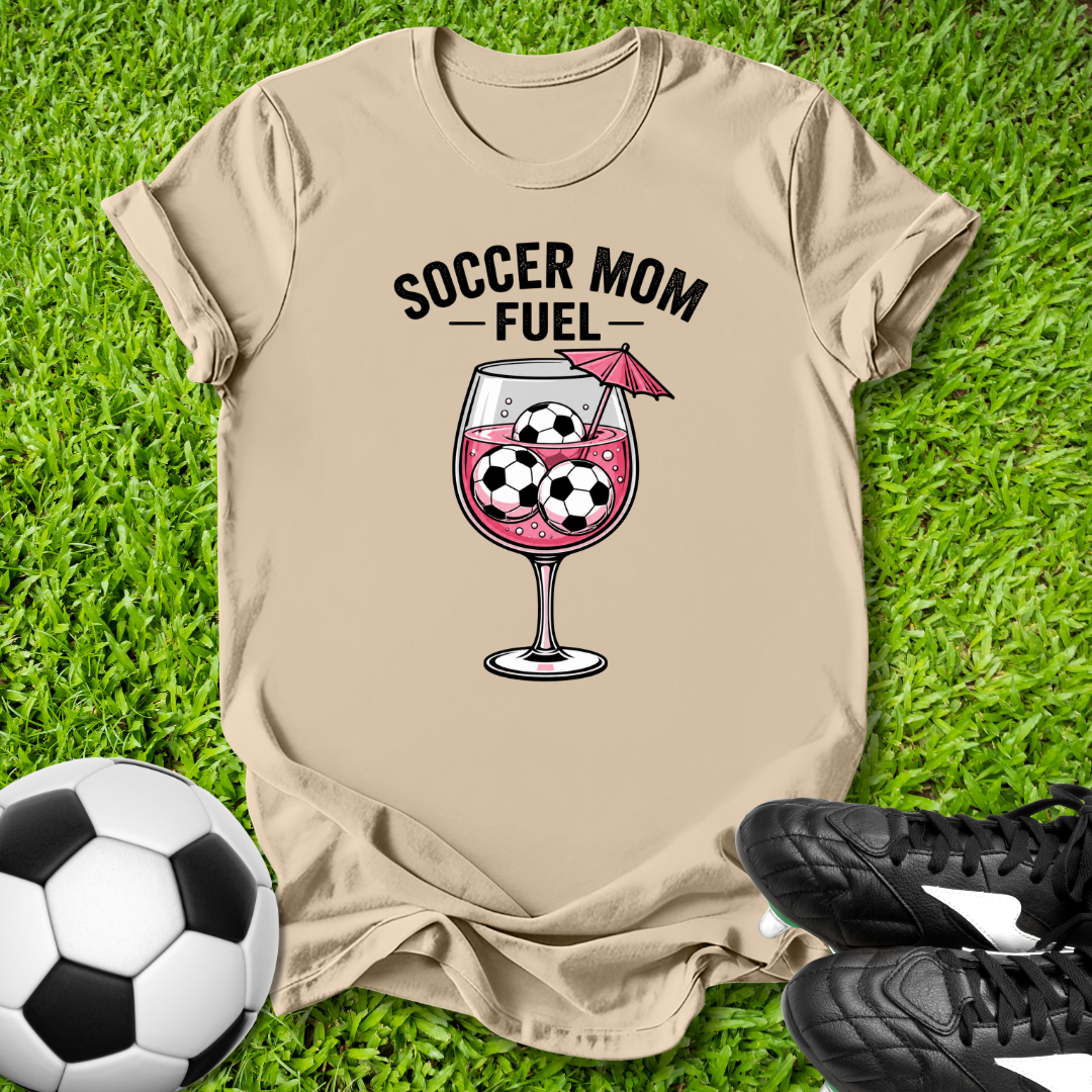 Beige t-shirt with 'Soccer Mom Fuel' graphic on grass with soccer ball and cleats.