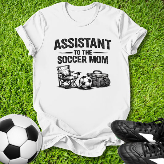 White t-shirt with 'Assistant to the Soccer Mom' graphic on grass with soccer ball and cleats.
