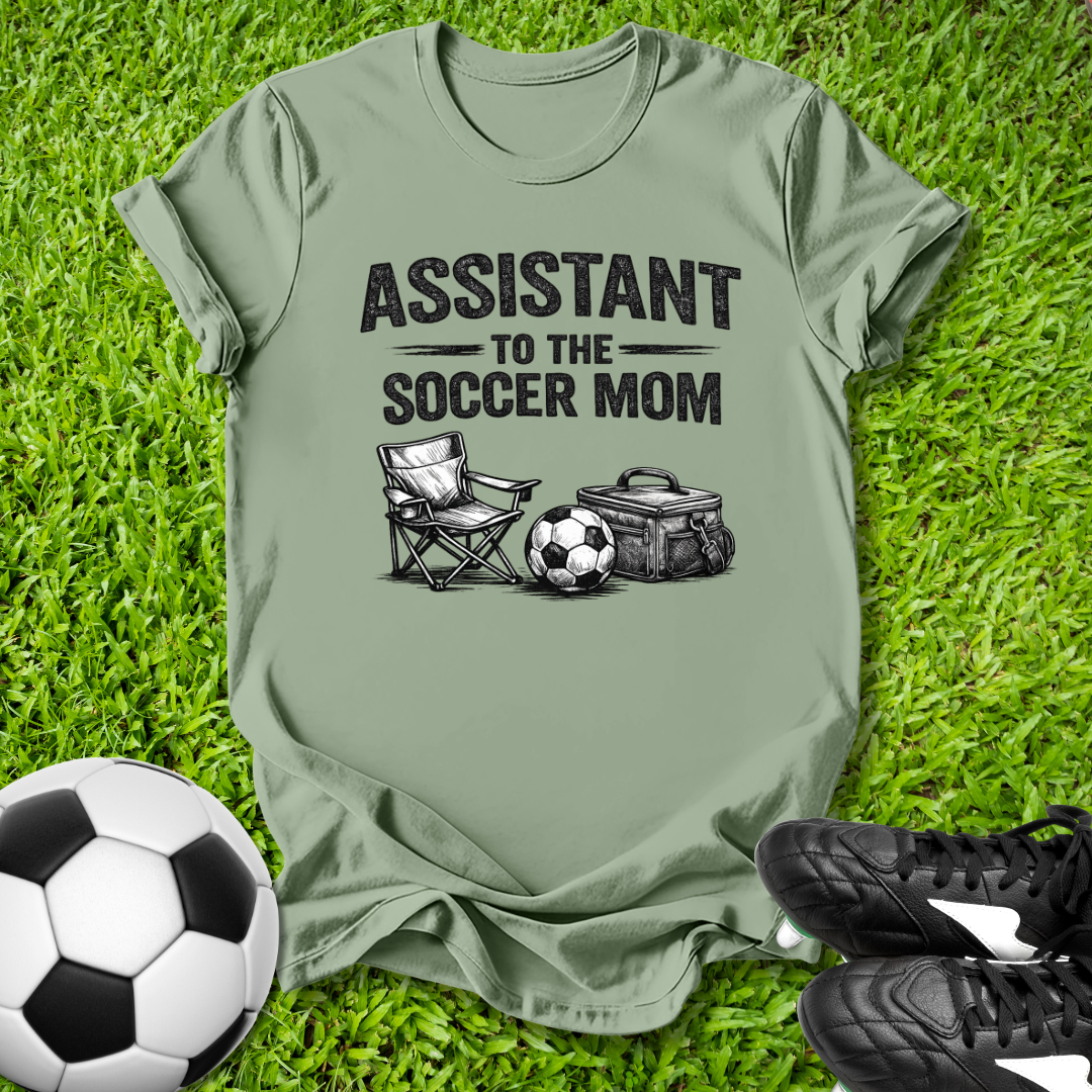 Green t-shirt with 'Assistant to the Soccer Mom' text and graphics on grass with soccer ball and shoes.