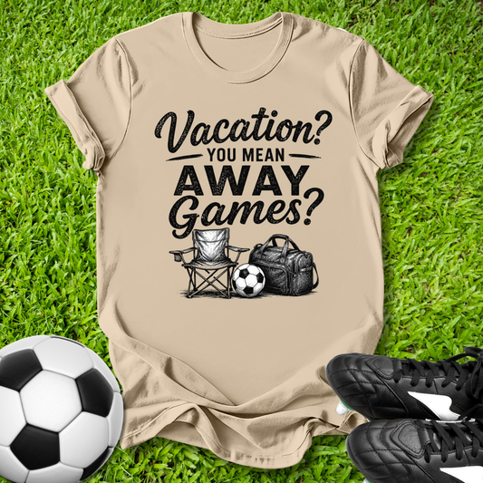 Beige t-shirt with 'Vacation? You Mean Away Games?' text on grass with soccer ball and shoes.