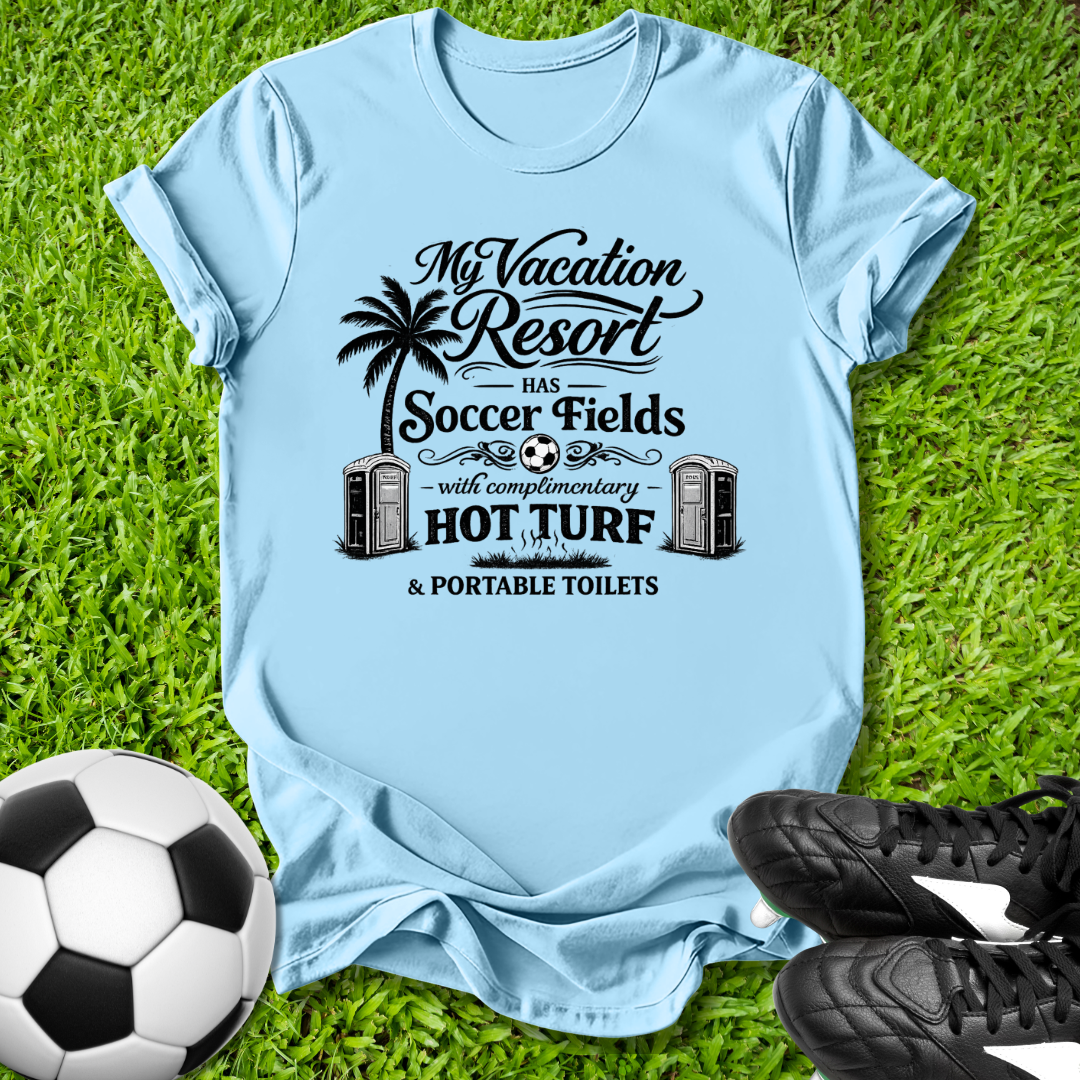 Light blue t-shirt with humorous graphic and text on grass with soccer ball and shoes.