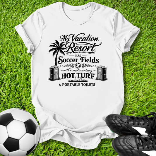 White t-shirt with a humorous soccer-themed design on grass with a soccer ball and shoes.