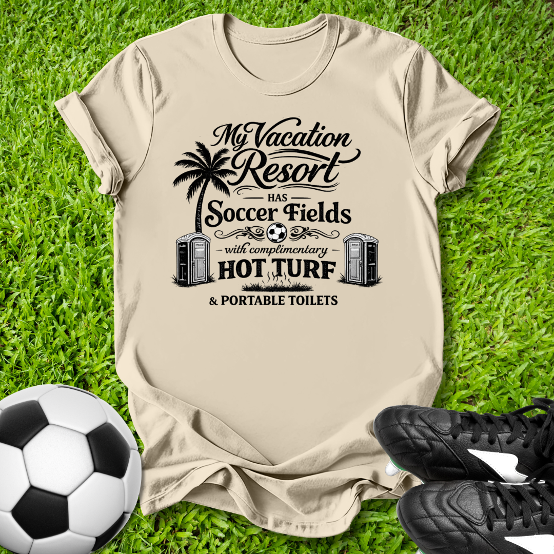 Beige t-shirt with a humorous soccer-themed graphic on grass with a soccer ball and shoes.