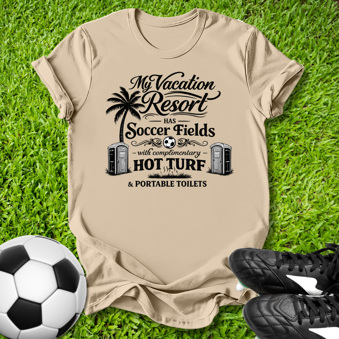 Beige t-shirt with a humorous soccer-themed graphic on grass with a soccer ball and shoes.