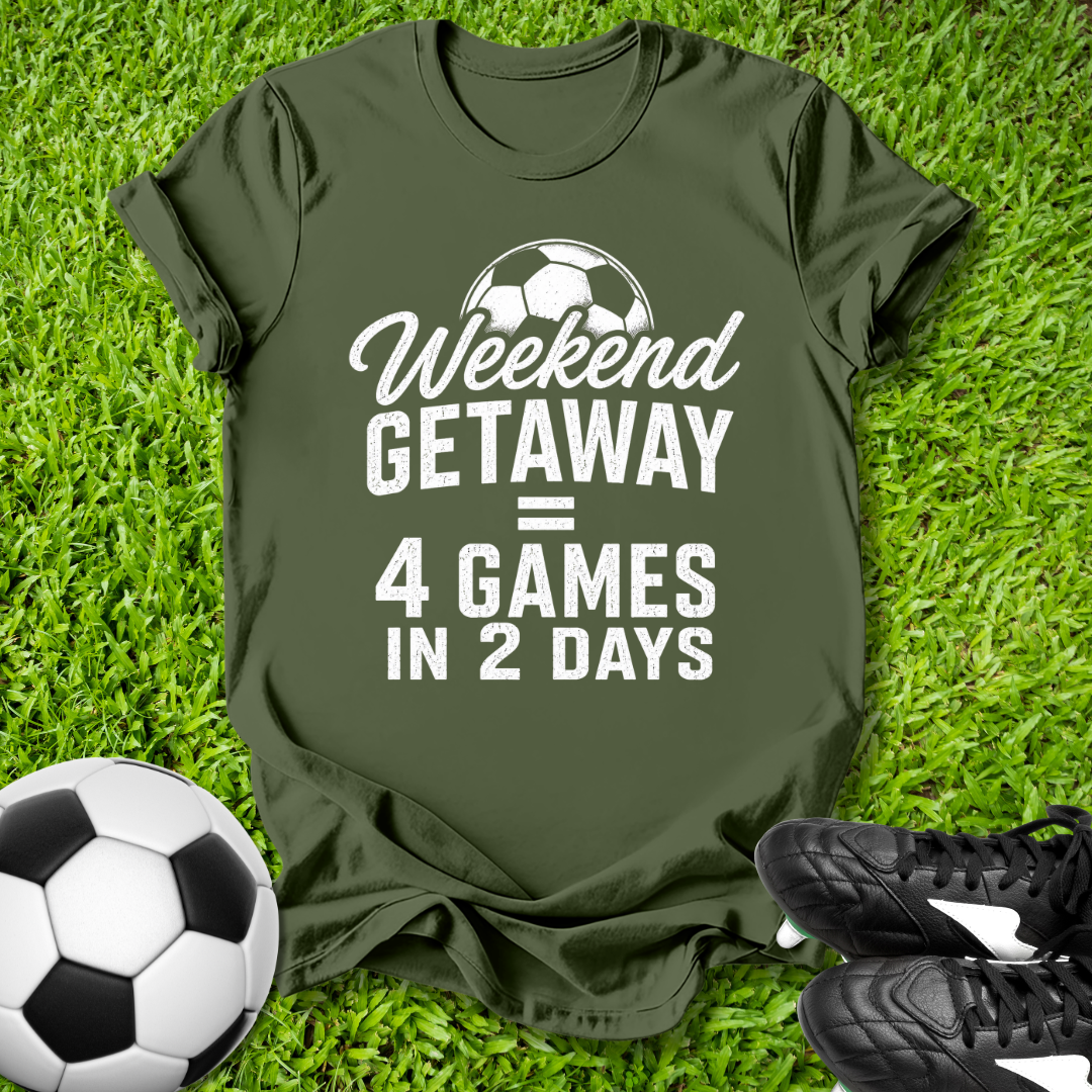 Green t-shirt with 'Weekend Getaway = 4 Games in 2 Days' text on grass with soccer ball and shoes.
