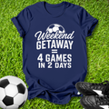 Navy blue t-shirt with 'Weekend Getaway = 4 Games in 2 Days' text on grass with soccer ball and shoes.