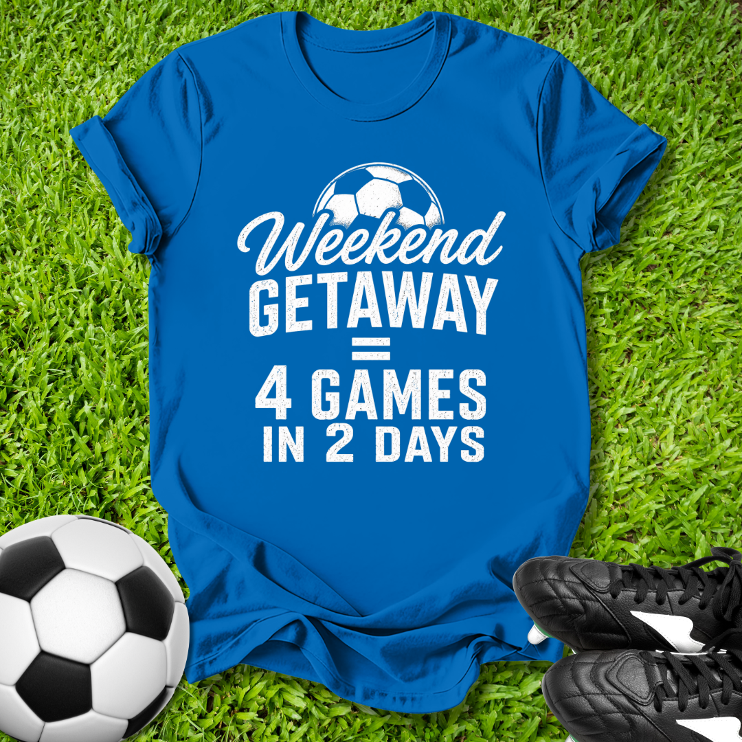 Blue t-shirt with 'Weekend Getaway = 4 Games in 2 Days' text on grass with soccer ball and shoes.
