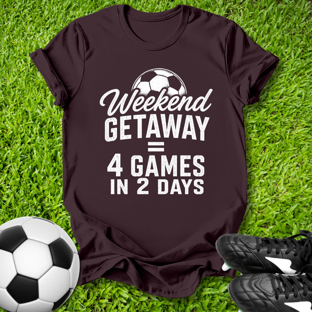 Brown t-shirt with 'Weekend Getaway = 4 Games in 2 Days' text on grass with soccer ball and shoes.