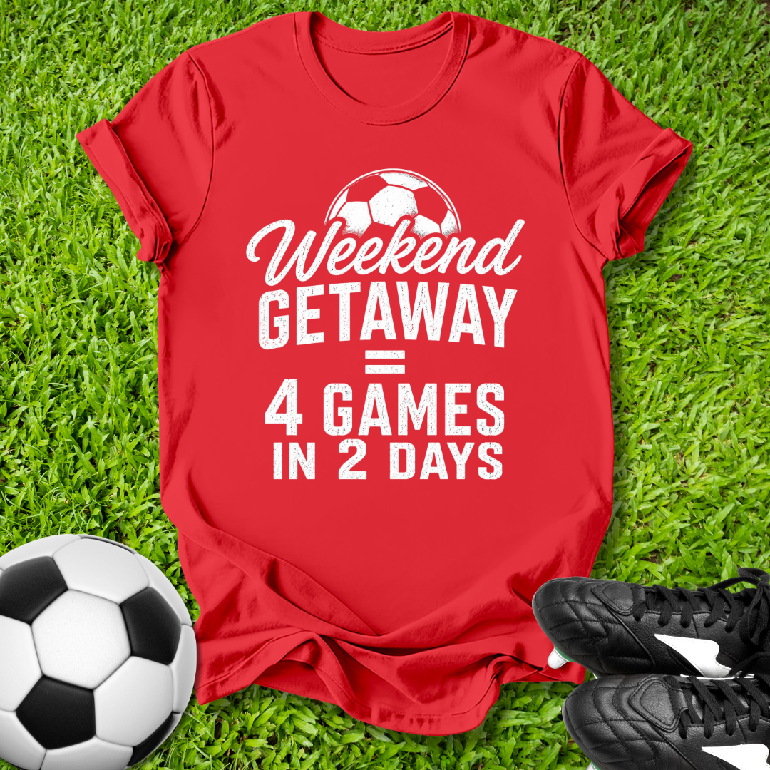 Red t-shirt with 'Weekend Getaway = 4 Games in 2 Days' text on grass with soccer ball and shoes.