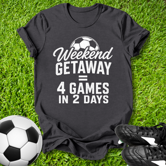 Black t-shirt with 'Weekend Getaway = 4 Games in 2 Days' text on grass with soccer ball and shoes.