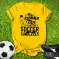 Yellow t-shirt with 'My Summer Tan Comes from Soccer Complexes' text on grass with soccer ball and shoes.