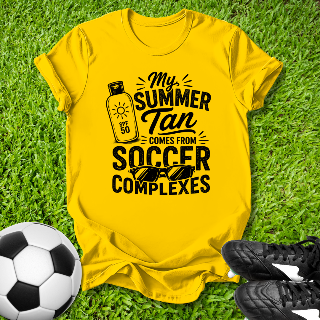 Yellow t-shirt with 'My Summer Tan Comes from Soccer Complexes' text on grass with soccer ball and shoes.