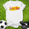 White t-shirt with 'Soccer Mom' text on grass with soccer ball and shoes