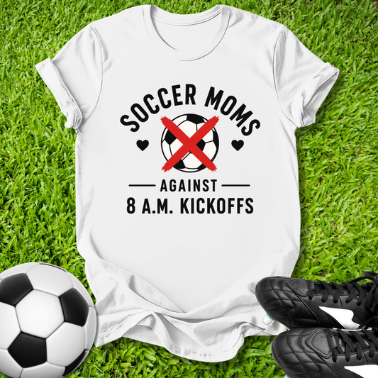 White t-shirt with 'Soccer Moms Against 8 A.M. Kickoffs' design on grass with soccer ball and shoes.