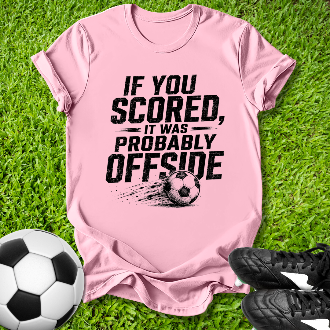 Pink t-shirt with offside soccer-themed text on grass with soccer ball and shoes