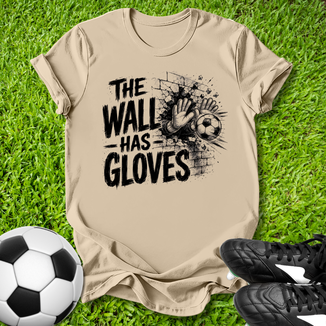Beige t-shirt with 'The Wall Has Gloves' graphic on grass with soccer ball and shoes.