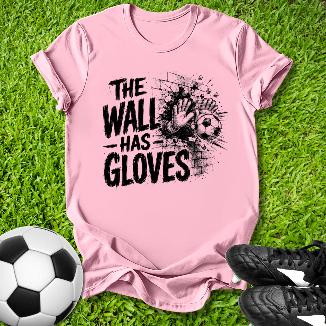 Pink t-shirt with 'The Wall Has Gloves' graphic on grass with soccer ball and shoes.