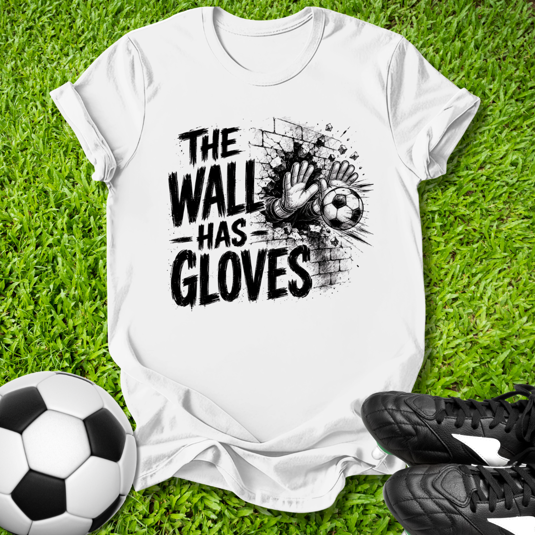 White t-shirt with 'The Wall Has Gloves' graphic on grass with soccer ball and shoes.