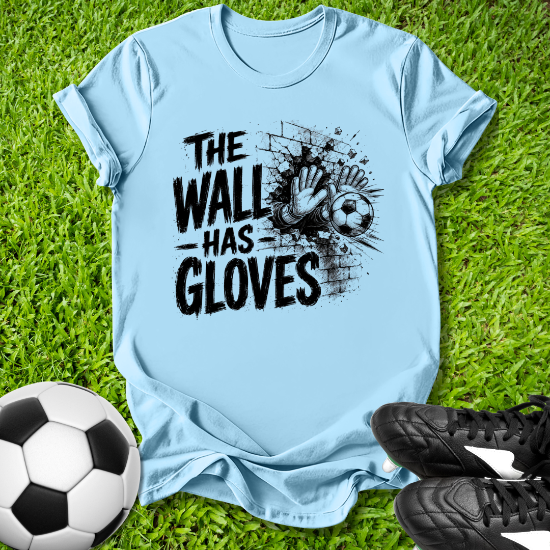 Light blue t-shirt with 'The Wall Has Gloves' graphic on grass with soccer ball and shoes.