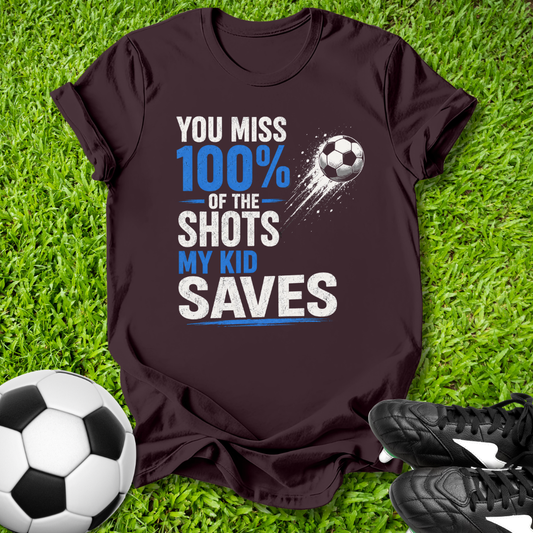 Dark brown t-shirt with soccer-themed text on grass with soccer balls and shoes.