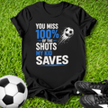 Black t-shirt with soccer-themed text on grass with soccer ball and shoes
