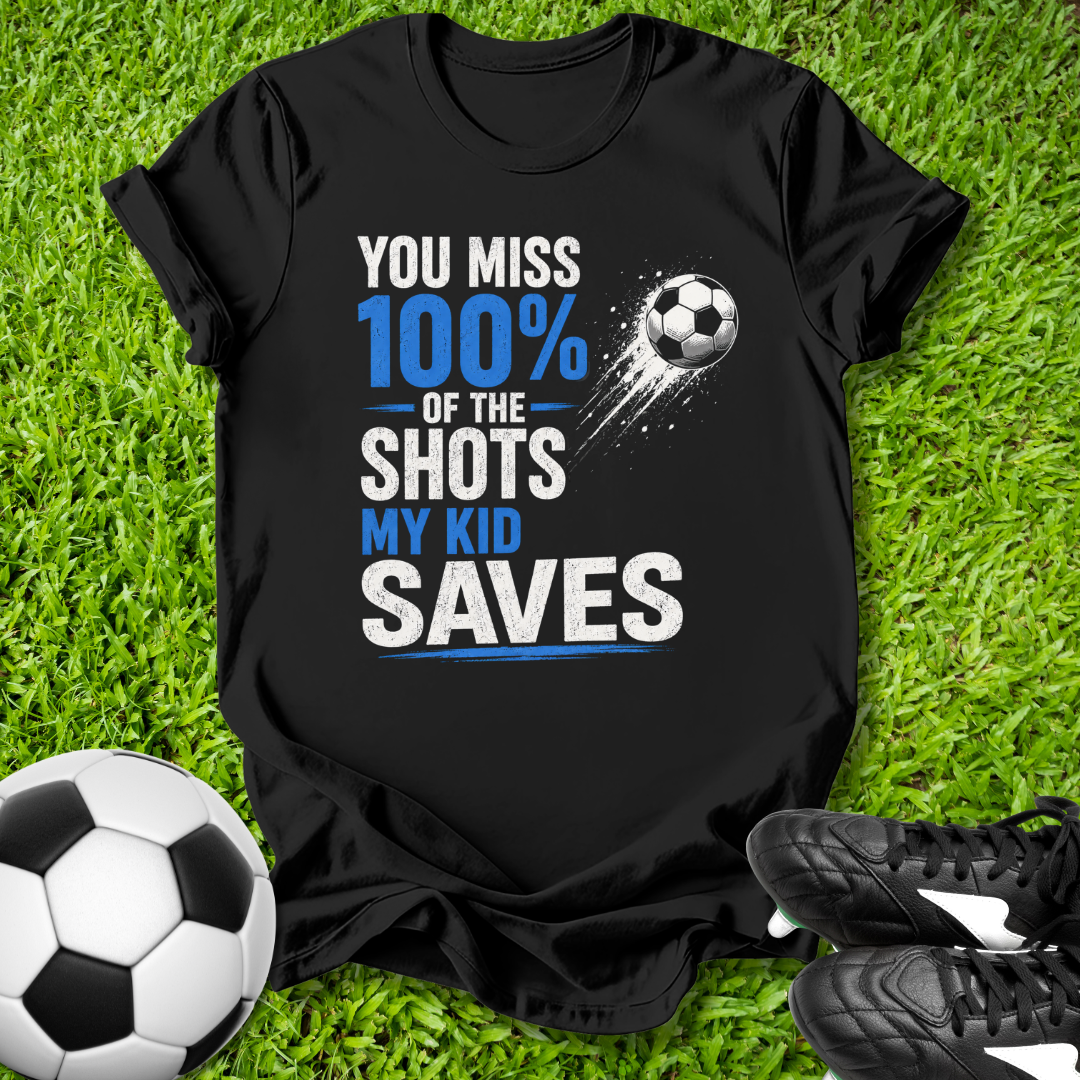 Black t-shirt with soccer-themed text on grass with soccer ball and shoes