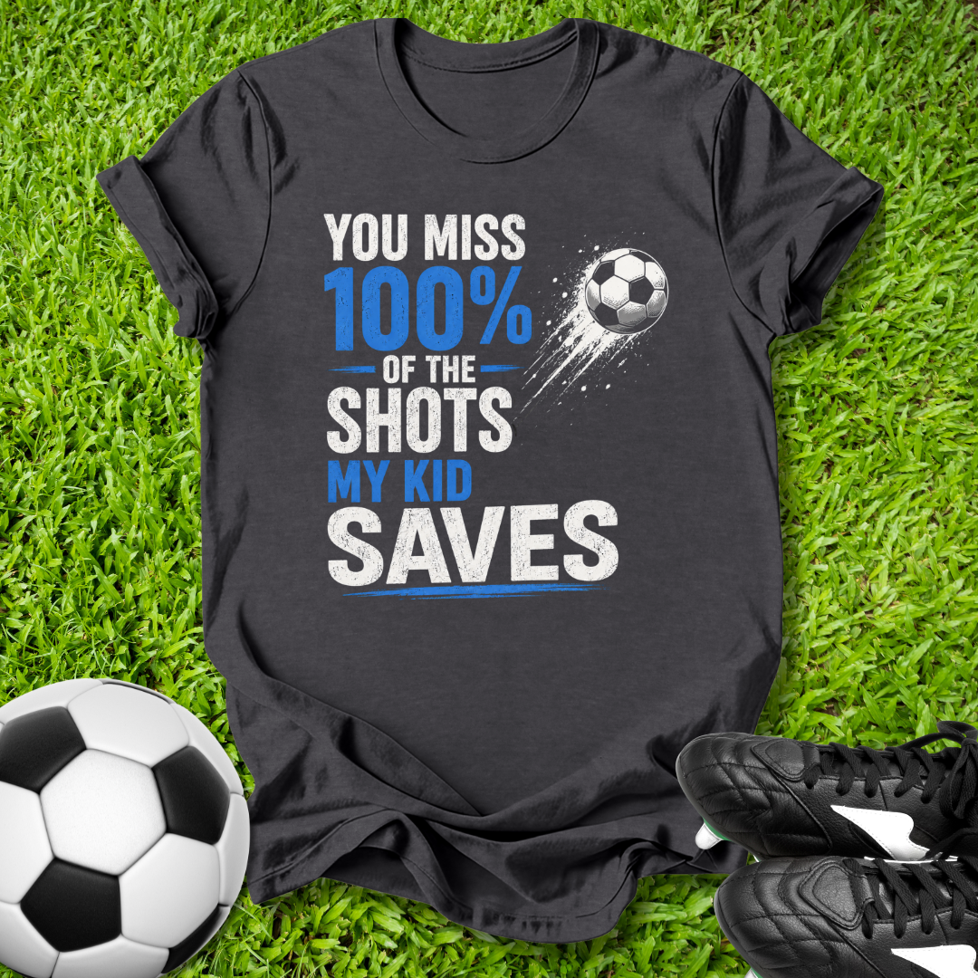 Black t-shirt with soccer-themed text on grass with soccer balls and shoes.