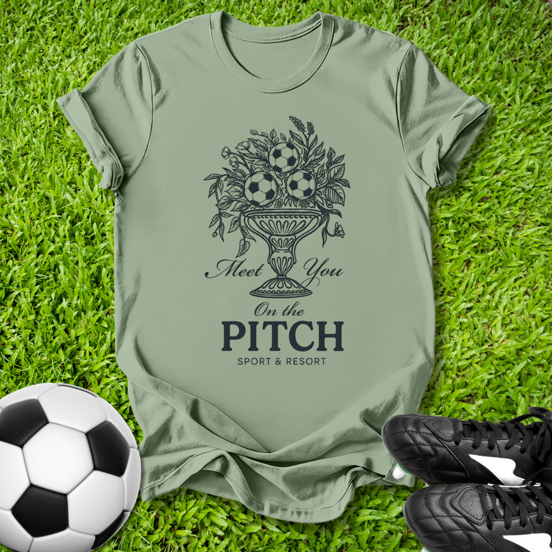 Green t-shirt with soccer-themed design on grass with soccer ball and shoes