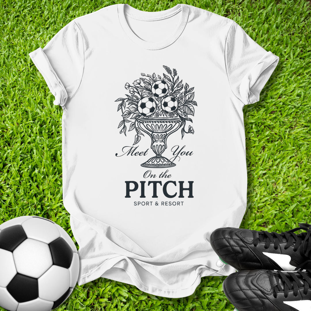 White t-shirt with sports-themed design on grass with soccer ball and cleats
