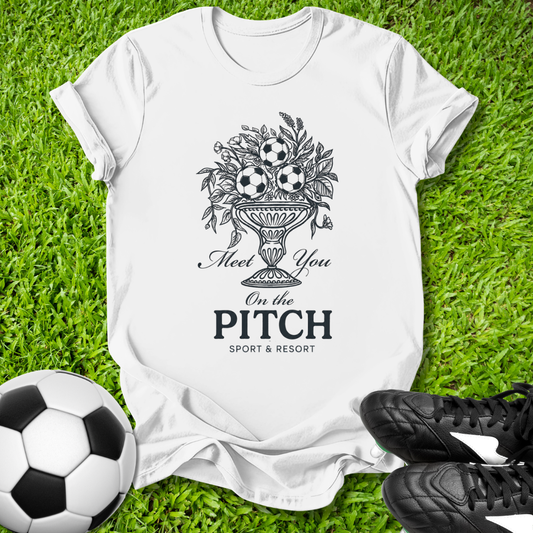 White t-shirt with sports-themed design on grass with soccer ball and cleats