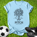 Light blue t-shirt with sports-themed design on grass with soccer ball and shoes.