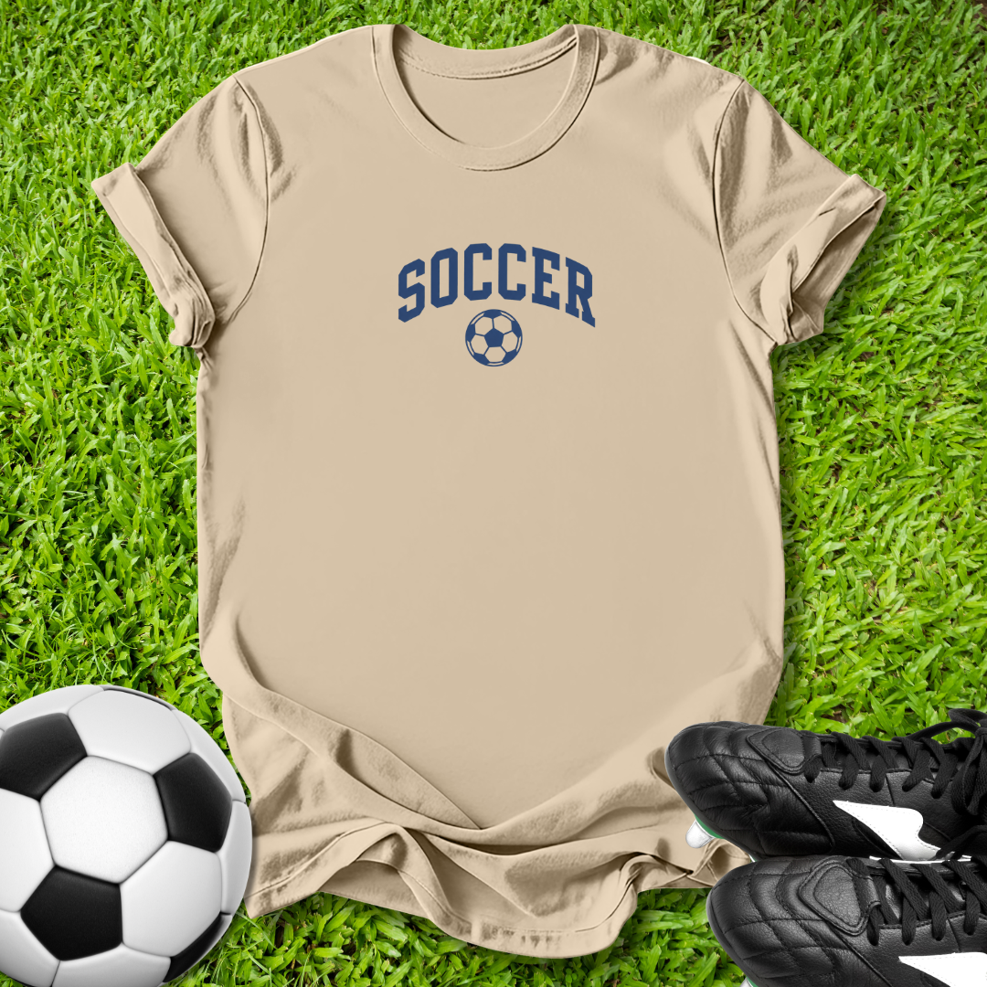 Beige t-shirt with 'SOCCER' text on grass with soccer ball and shoes