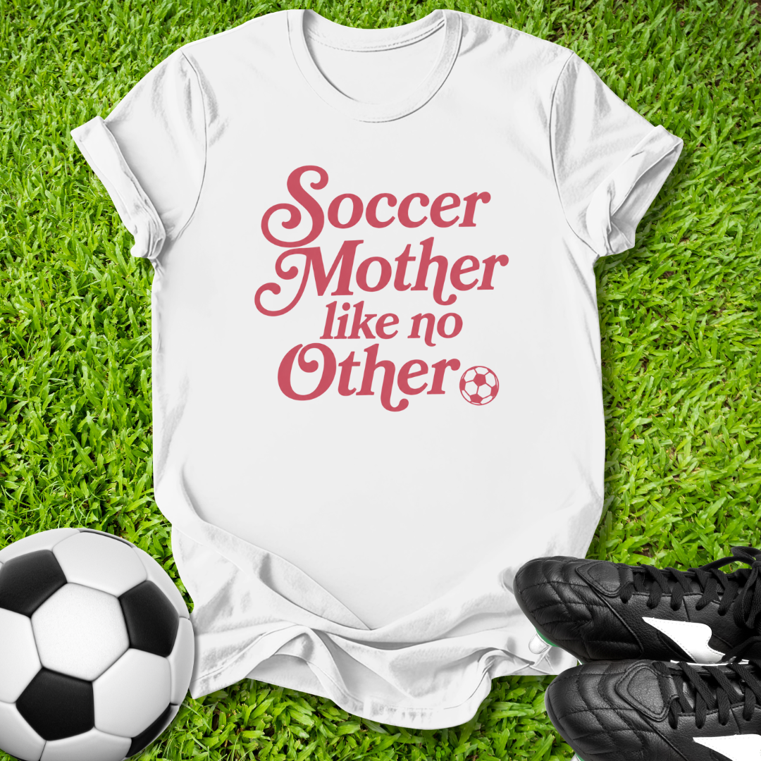 White t-shirt with 'Soccer Mother like no Other' text on grass with soccer ball and shoes.