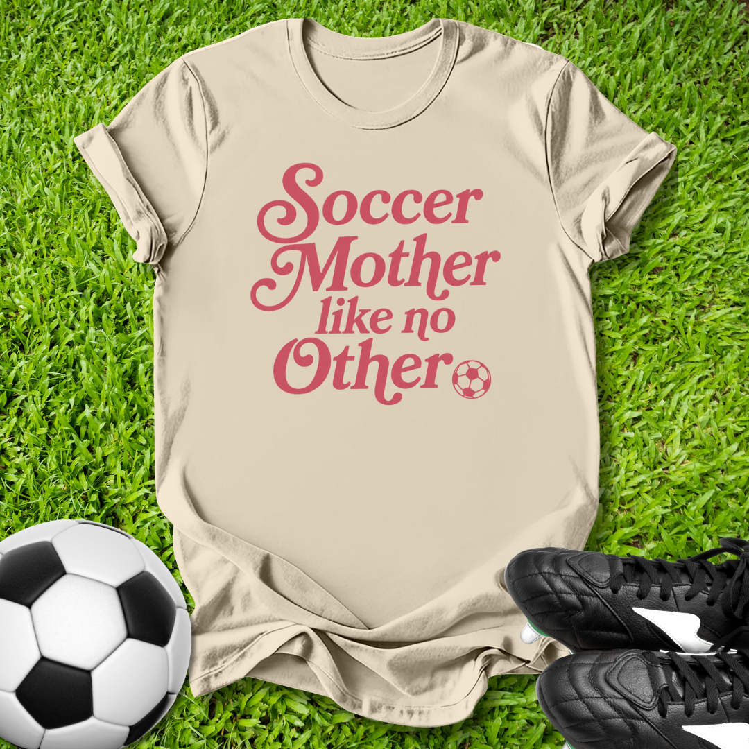 Beige t-shirt with 'Soccer Mother like no Other' text on grass with soccer ball and shoes.