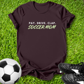Maroon t-shirt with 'PAY. DRIVE. CLAP. SOCCERMOM' text on grass with soccer ball and shoes.