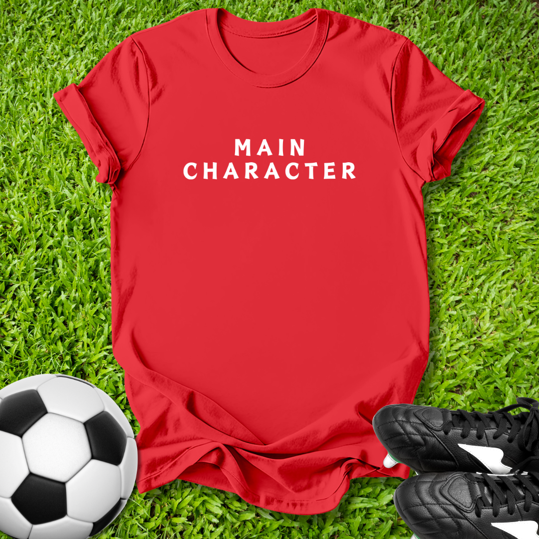 Red t-shirt with 'MAIN CHARACTER' text on grass with soccer ball and shoes